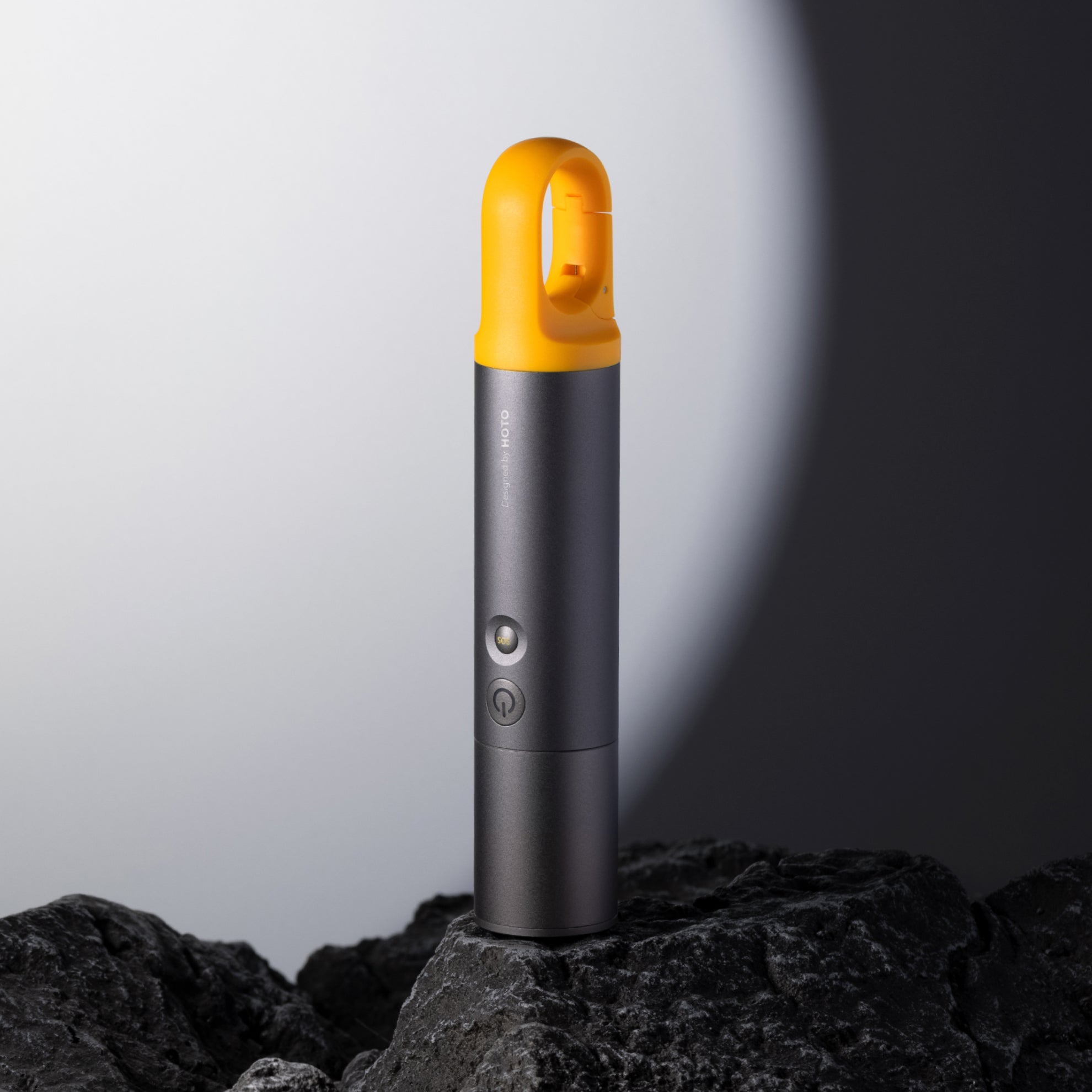 A portable handheld flashlight with a gray body and yellow cap, displayed on a textured surface, with a focus beam in the background.
